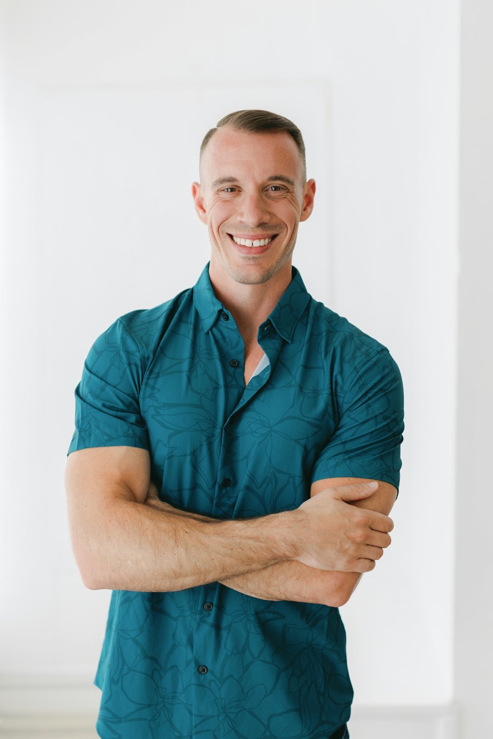 Man wearing a teal patterned shirt standing with arms crossed.
