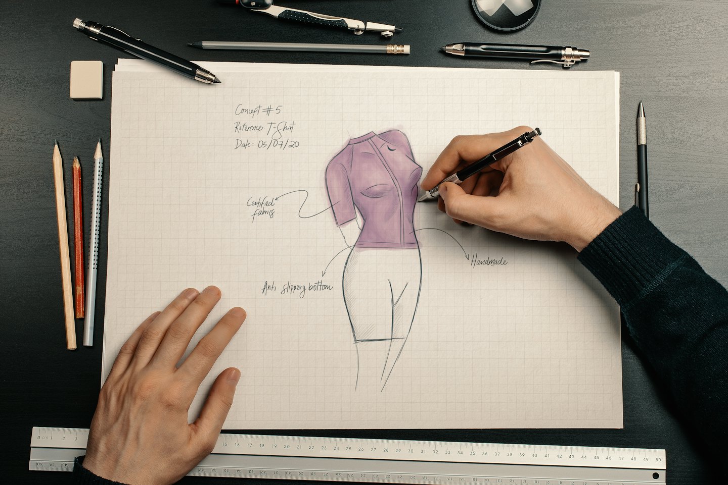 Hands sketch a purple athletic shirt on grid paper.