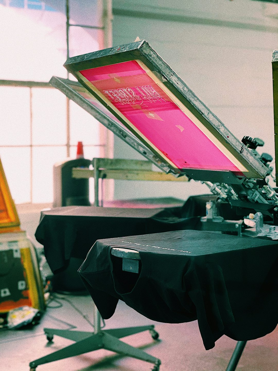 Screen printing press with pink design on t-shirt.
